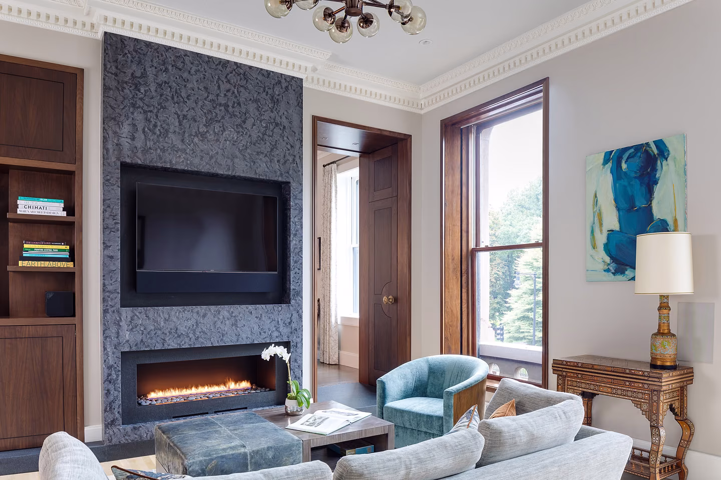 An ornate cornice and tall cased window hold their place beside a clean-lined contemporary fireplace wall.